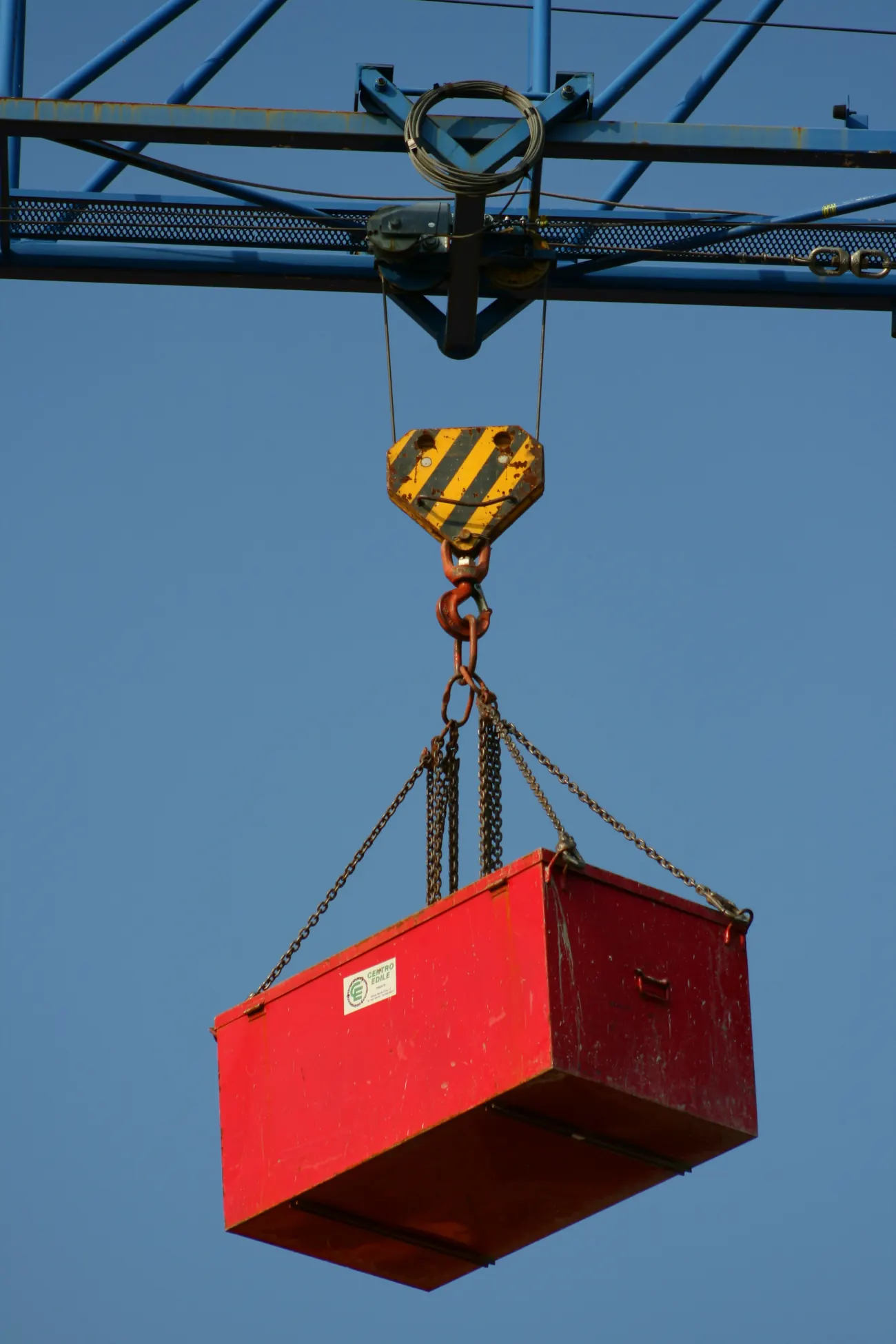 Red load box rigged with chains hanging from a crane hook